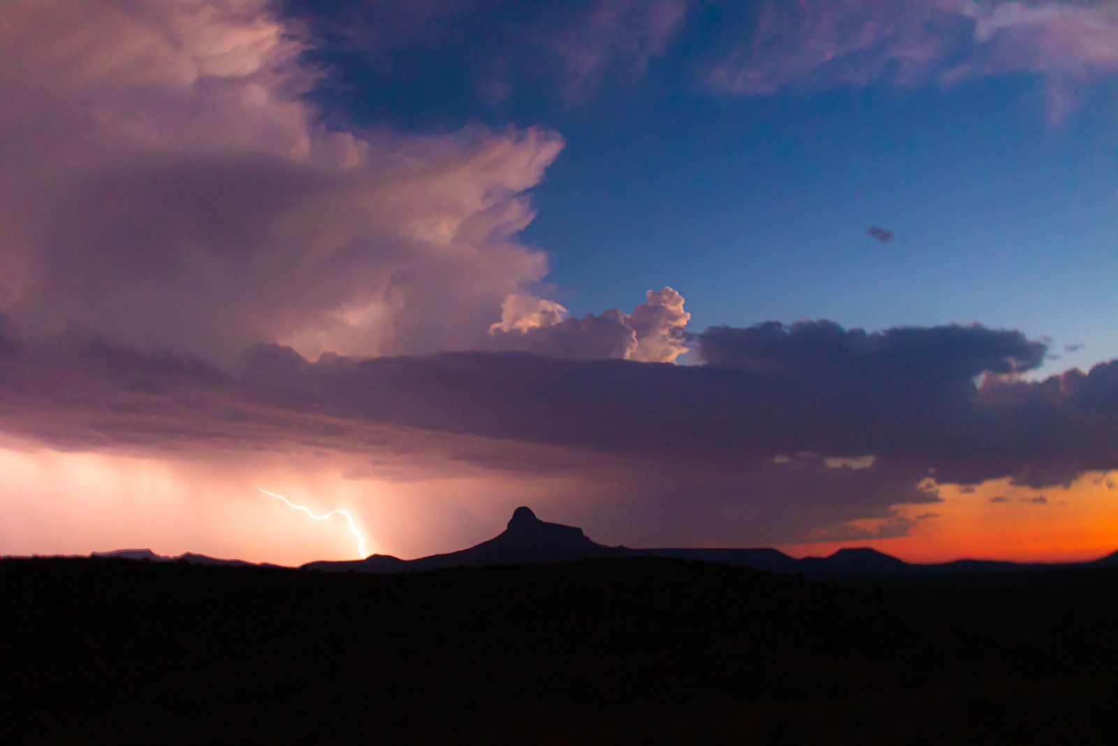 Storm light and distant lightning over a desert ridgeline