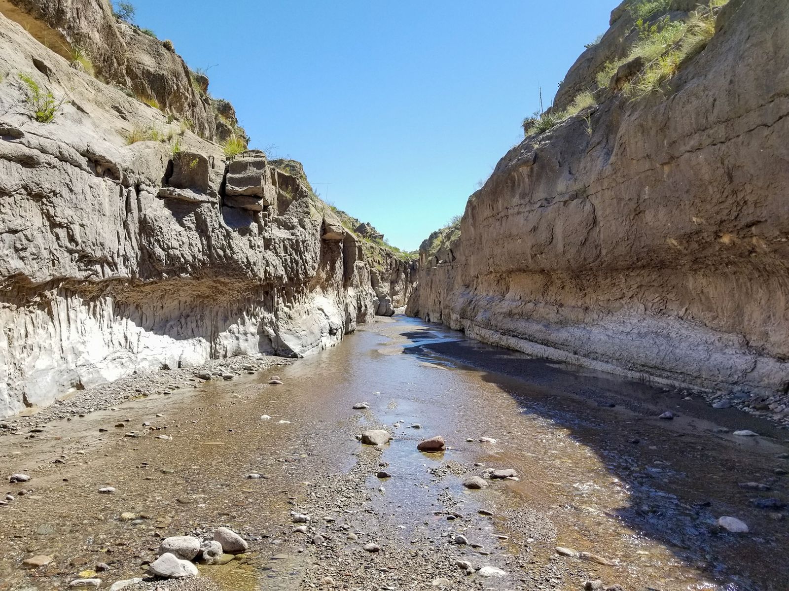 Shallow river running between banded canyon cliffs