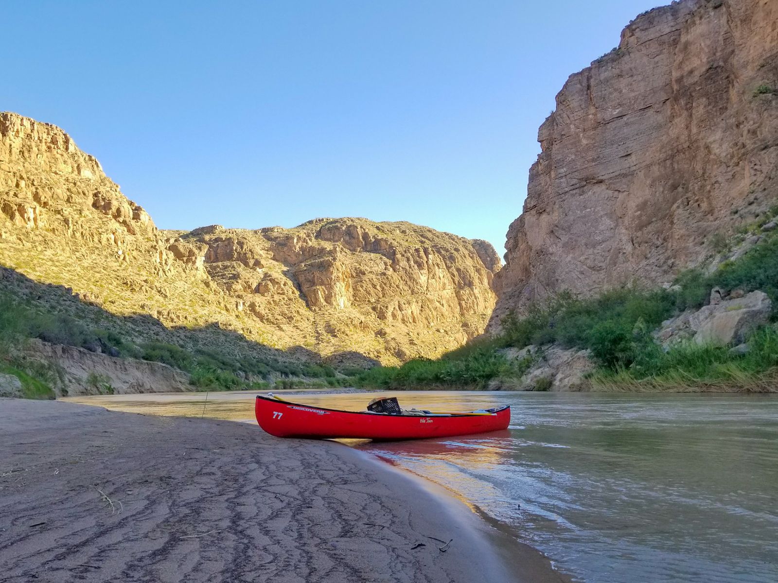Red canoe pulled up on a sandbar inside a canyon