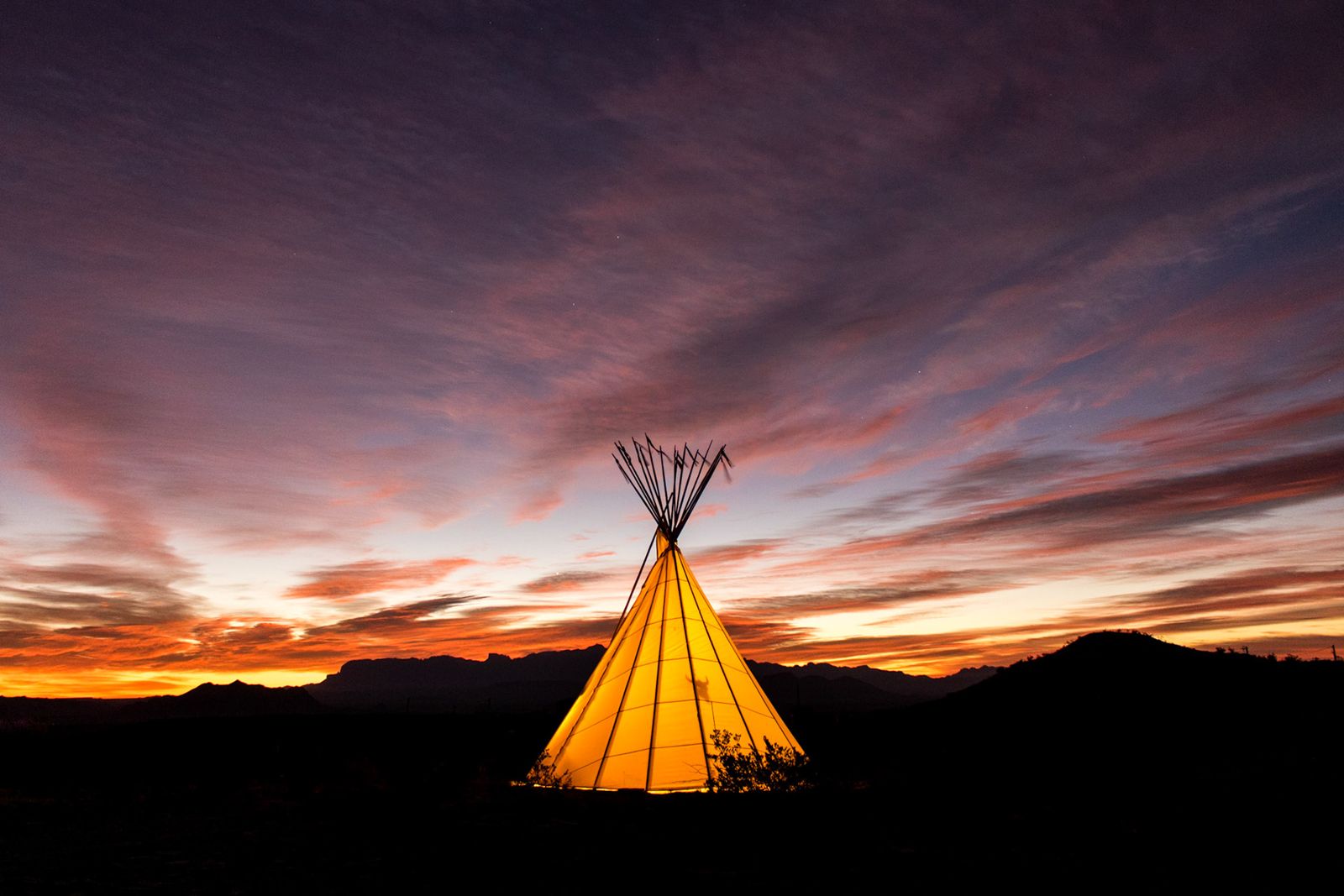 Teepee frame silhouetted against an orange sunset